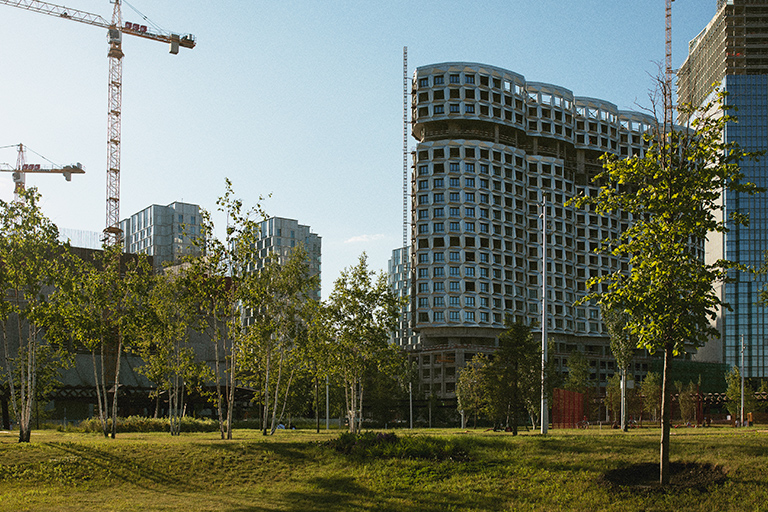 Construção de prédios com uma área verde repleta de árvores à frente.